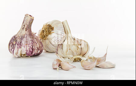 Close-up still life of three red garlic bulbs, two whole and one open with its cloves in front, on a white background Stock Photo