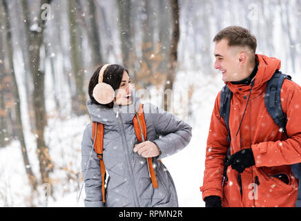 Boy and girl with backpacks walking at the winter snowy forest and laughing of the good joke Stock Photo