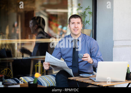 Businessman relaxing at cafe terrace in the morning drinking coffee and reading financial newspaper Stock Photo