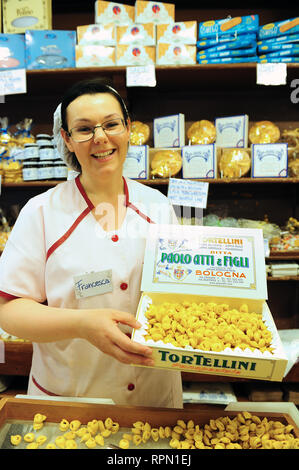 Female shop assistant holding a vintage-looking box of tortellini pasta at Paolo Atti, a famous deli shop in Bologna, Italy Stock Photo