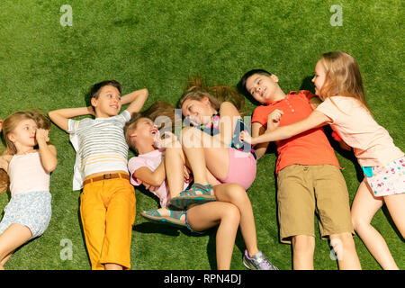 Group of happy children playing outdoors. Kids having fun in spring park. Friends lying on green grass. Top view portrait Stock Photo