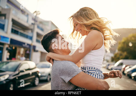 Smiling young man holding his girlfriend in his arms while having a good time together in the city Stock Photo