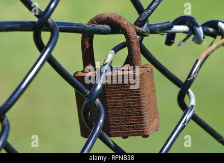 Dirty old corrosive padlock on wire mesh fence Stock Photo