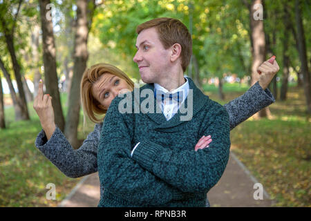 Couple is quarrelling because of the disagreements between them in park. Woman showing middle finger Stock Photo