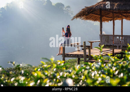 Woman wearing hill tribe dress sitting on the hut in green tea field. Stock Photo