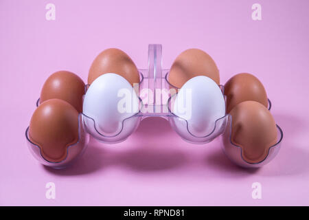 White and brown chicken eggs in a plastic package, on a pink background Stock Photo