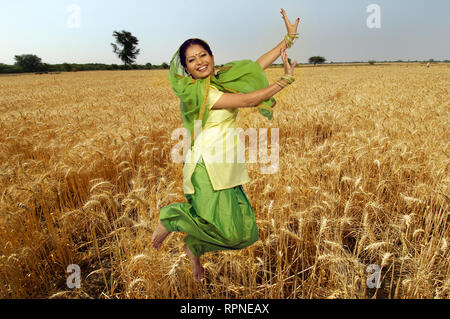 PORTRAIT OF A SARDARNI, SIKH WOMAN JUMPING DANCING THE BHANGRA WITH WHEAT FIELDS IN THE BACKGROUND Stock Photo