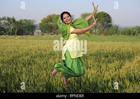 PORTRAIT OF A SARDARNI, SIKH WOMAN JUMPING DANCING THE BHANGRA WITH WHEAT FIELDS IN THE BACKGROUND Stock Photo