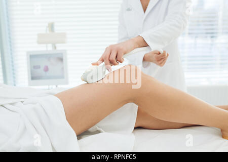 Unrecognizable female cosmetologist doing Rf lifting procedure on woman s long slim legs in a beauty parlor. Treatment of overweight and flabby skin. Stock Photo