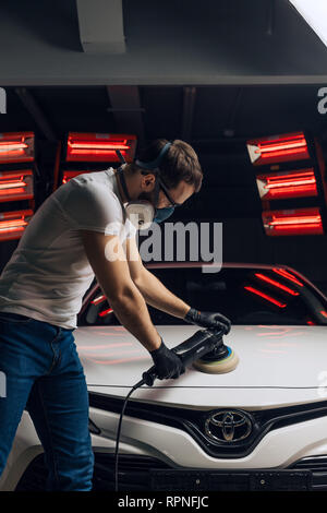 young man in mask using an auto tool after painting the car. close up side view photo Stock Photo