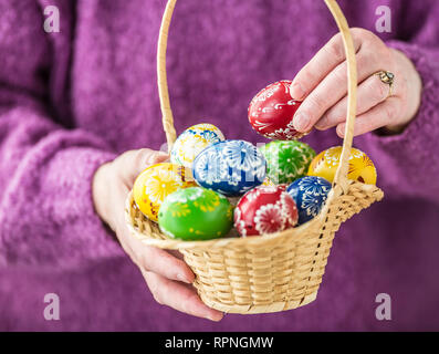 Basket full of multicolored easter eggs in hands pensioner woman. Stock Photo