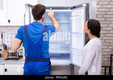 Young Woman Looking At Male Serviceman Checking Temperature Of Refrigerator Stock Photo