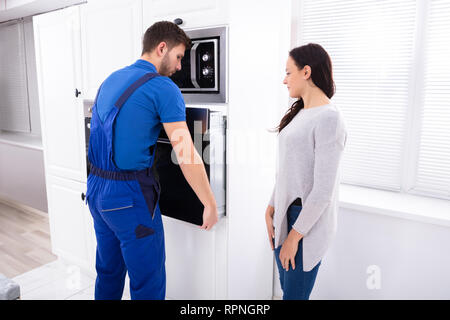 Beautiful Woman Looking At Young Serviceman Installing Oven In Kitchen Stock Photo