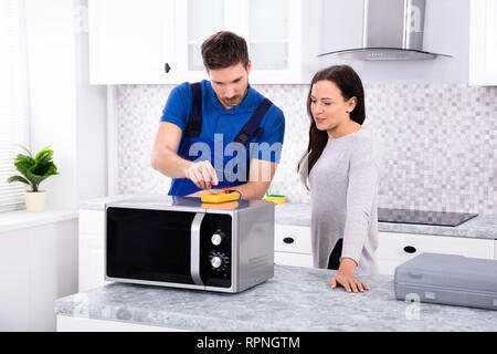 Pretty Woman Standing Near Repairman Repairing Oven Using Digital Multimeter In Kitchen Stock Photo