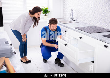 Woman Looking At Male Handyman Installing Door Of Drawer In The Kitchen Stock Photo