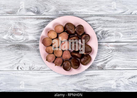 Fresh lychee an chestnuts on the plate on a wooden background. Stock Photo