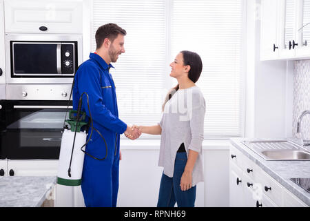 Woman Showing Thumbs Up With Pest Control Worker Standing In Kitchen Stock Photo