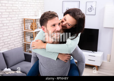 Portrait Of A Happy Young Man Giving Piggyback To His Wife At Home Stock Photo