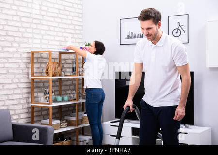 Side View Of Two Persons Cleaning The Shelf And Mopping Floor In The Living Room Stock Photo