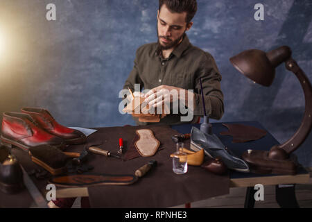 man performs restoration of old shoes in the room with blue wall Stock Photo