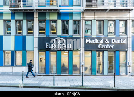 City of Brussels / Belgium - 02 15 2019: Pedestrian passing by the facade of the Eurocare office with rectangular blue shapes and glass Stock Photo