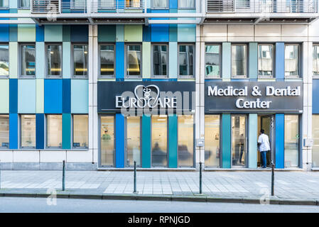 City of Brussels / Belgium - 02 15 2019: Male nurse deliveringand standing at the facade of the Eurocare office with rectangular blue shapes and glass Stock Photo