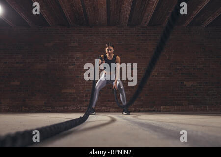 Active fit female athlet is doing battle rope exercise while working out at cross-fit training, low angle distant shot Stock Photo