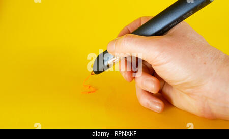 a man's hand draws with a 3d printer pen on a yellow background, footage ideal for topics such as innovation, technology Stock Photo