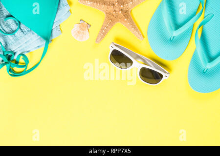 Blue flip flops, swimsuit, sunglasses and starfish on yellow background. Stock Photo