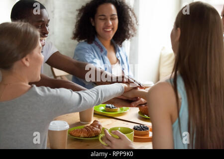 Happy smiling multiracial friends joining hands at meeting in cafe Stock Photo