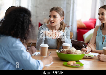 Attractive girl sharing ideas, doing homework with friends in cafe Stock Photo