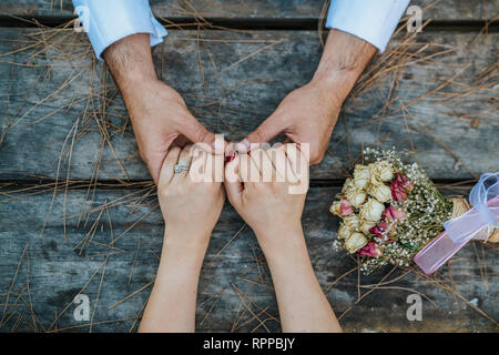 Wedding couple holding hands on wooden table with bouquet Stock Photo