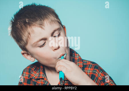 A cute boy in a pajamas brushes teeth with toothpaste before bedtime on a blue background 2019 Stock Photo