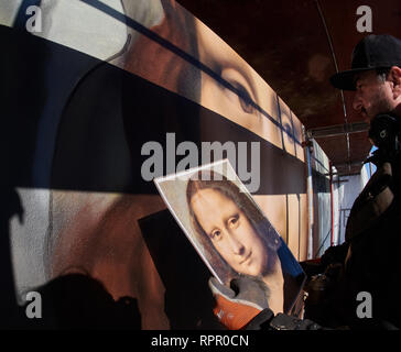 Berlin, Germany. 22nd Feb, 2019. The artist Tank stands high up on the scaffold, opposite the East Side Gallery and looks at his model. Together with the Berlin artist collective Die Dixons, he paints the oversized Mona Lisa on the windowless façade of the East Side Hotel. Credit: Annette Riedl/dpa/Alamy Live News Stock Photo