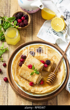 Healthy Pancakes breakfast. Stack of homemade thin pancakes or crepes on a rustic table, served with honey and fresh berries. Stock Photo