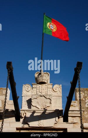Portuguese flag hoisted at the entrance of a fort in Lagos, Algarve, where you can also see the shield of Portugal engraved on the stone of the fort. Stock Photo