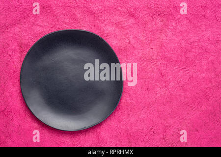 black ceramic plate with an irregular edge on a pink handmade Huun Mayan  paper  with a copy space Stock Photo
