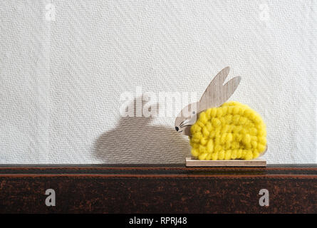 Yellow easter bunny in front of white wall in a room. Bunny decoration and white wallpaper background. Shadow of rabbit on the wall. Wooden bunny figu Stock Photo