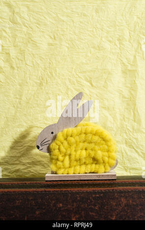 Yellow easter bunny in front of yellow paper wall. Bunny decoration. Shadow of rabbit on the wall. Wooden bunny figure shape and yellow yarn. Minimali Stock Photo