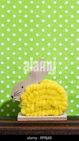 Yellow easter bunny in front of wall of points in a room. Bunny decoration and green wallpaper background on dots. Shadow of rabbit on the wall. Woode Stock Photo