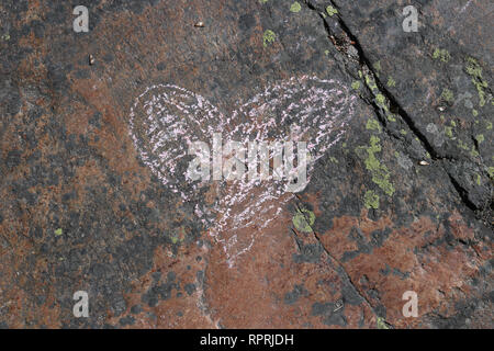 Cute pink heart drawn on a colorful rock surface. Beautiful red and black stone with green lichen on it. Romantic, cute symbol of loving and caring. Stock Photo