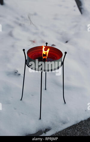 Big red candle burning with a big flame. Photographed outdoors during a cold snowy winter day in Finland. Beautiful home decor element. Stock Photo