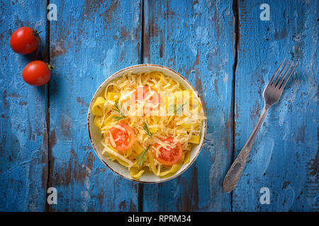 Pasta in a bowl with tomatoes and herbs on a blue old background
