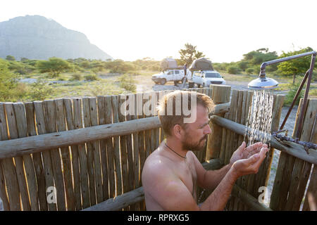 Western man stand under falling water drops, taking open style shower in outside bathroom in the camp of Tsodillo Hills, Botswana Stock Photo