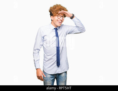 Young handsome business man with afro wearing glasses very happy and smiling looking far away with hand over head. Searching concept. Stock Photo