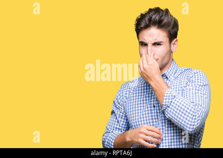 Young handsome business man over isolated background smelling something stinky and disgusting, intolerable smell, holding breath with fingers on nose. Stock Photo