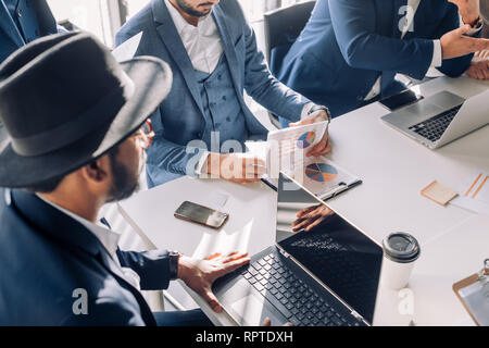 Multicultural business men meeting for analyzing profit reports using laptop, informaton from charts and graphs, making notes in note pads, close up Stock Photo