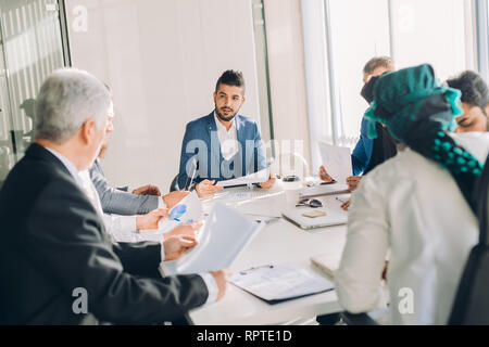 Young intelligent caucasian businessmen sharing his project ideas with executive business team creating plan, analyzing market and studying graphs cha Stock Photo