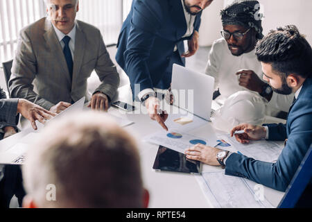 Multiracial group of male experts analyzing business resuls , close up of team with smartphones and tablet pc sitting at table in office, actively spe Stock Photo