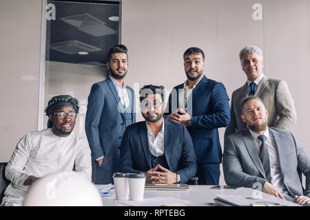 Diverse smiling business men gather at conference table together with his male Indian leader, attending meeting or corporate briefing. Arab and caucas Stock Photo